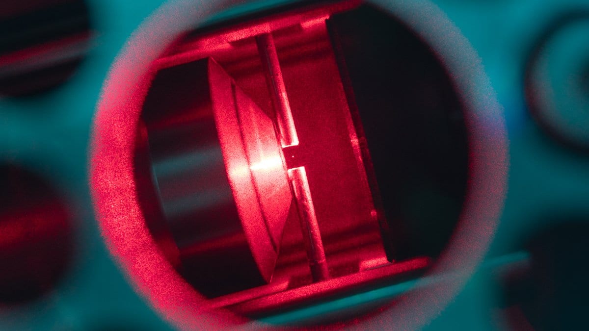 Close view of a laser trap, with red light filling a lens assembly inside a metal mount.