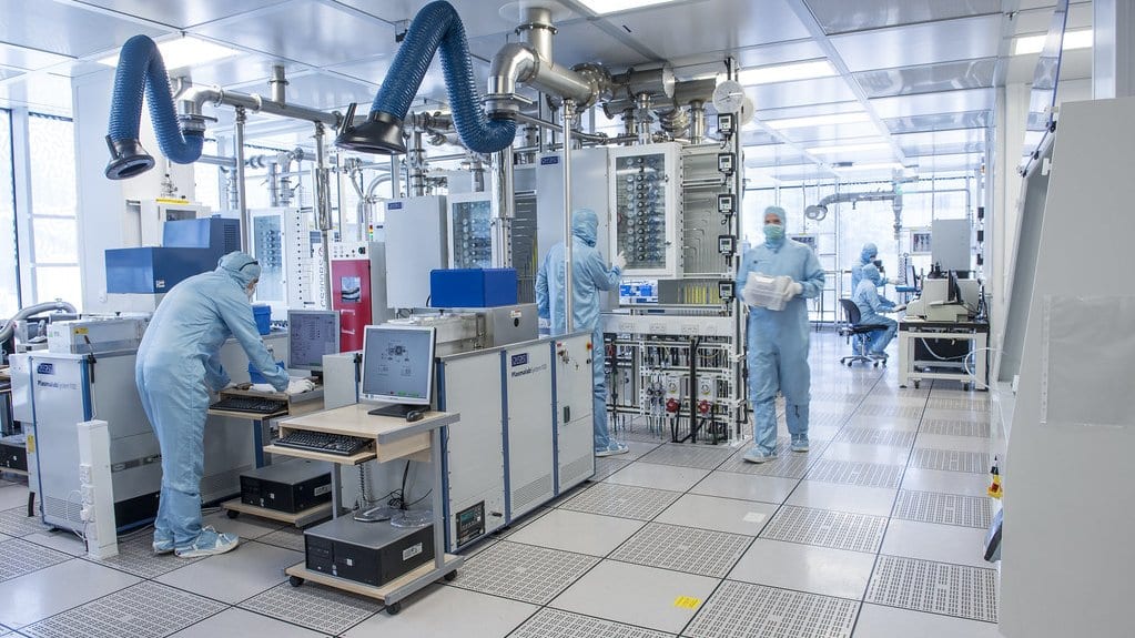 Researchers in blue cleanroom suits work at processing tools in a photonics nanofabrication laboratory.