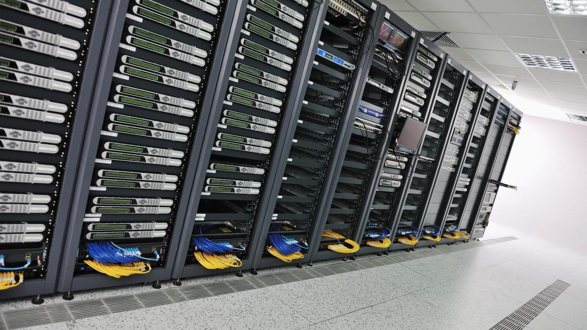 Rows of networked servers in a data hall, their ports linked by bundles of yellow and blue patch cables.