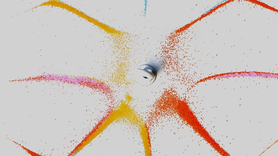 Orange, yellow, blue and pink powder on a gray plate forms a symmetric star pattern of curved lines around a small central driver.