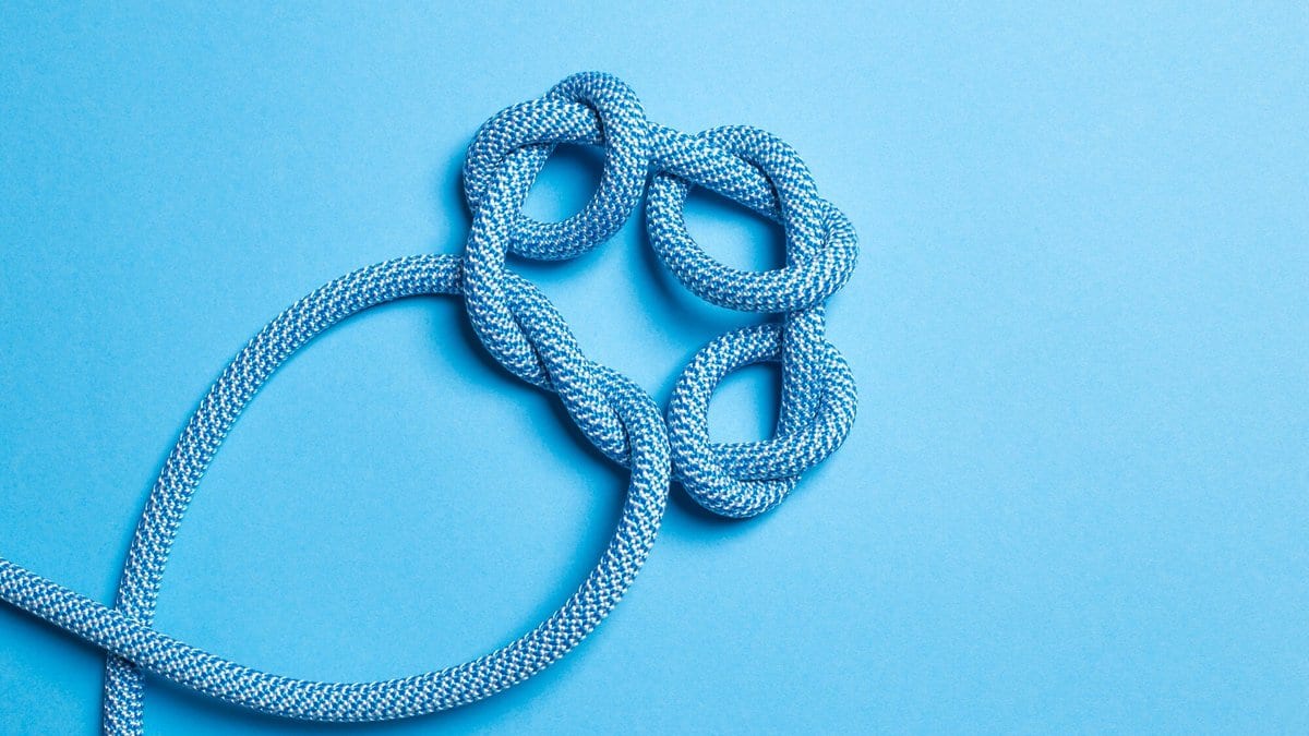 A length of blue climbing rope tied in a loose knot on a plain blue surface, the strand crossing over itself several times.