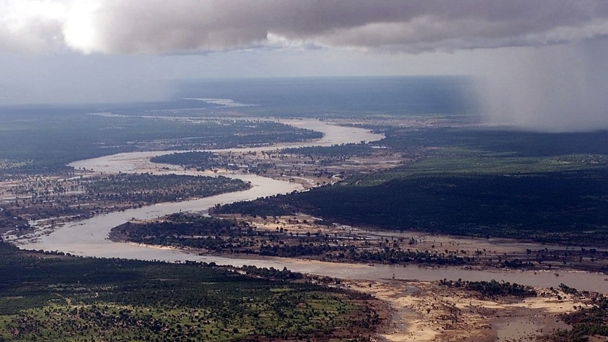 Aerial view of a dark shaft of rain falling from low cloud over the brown, swollen channels of the Limpopo River in southern Mozambique.
