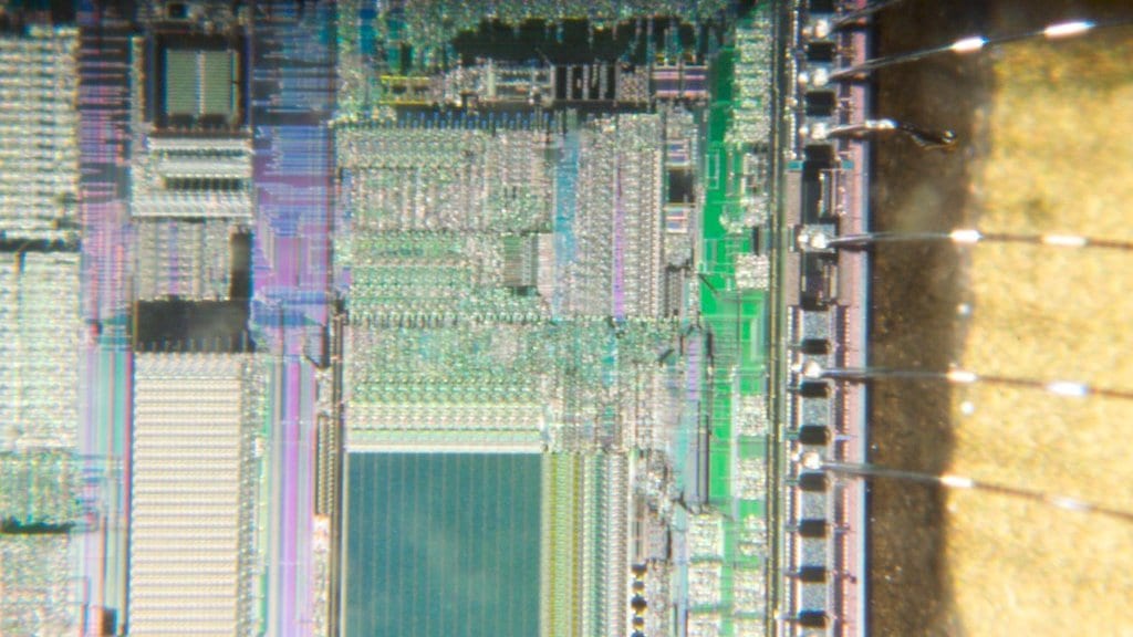 A decapsulated silicon chip seen under a microscope, with fine bond wires running from the edge of the die to the package pads.