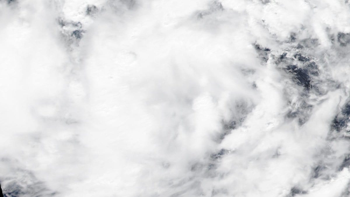 Satellite image of a dense tropical cyclone cloud mass over open water, with darker gaps of clear sky visible near the edges