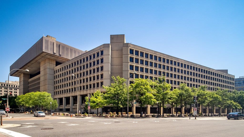 A large concrete federal office building occupying a city block in Washington, seen from across an empty intersection.