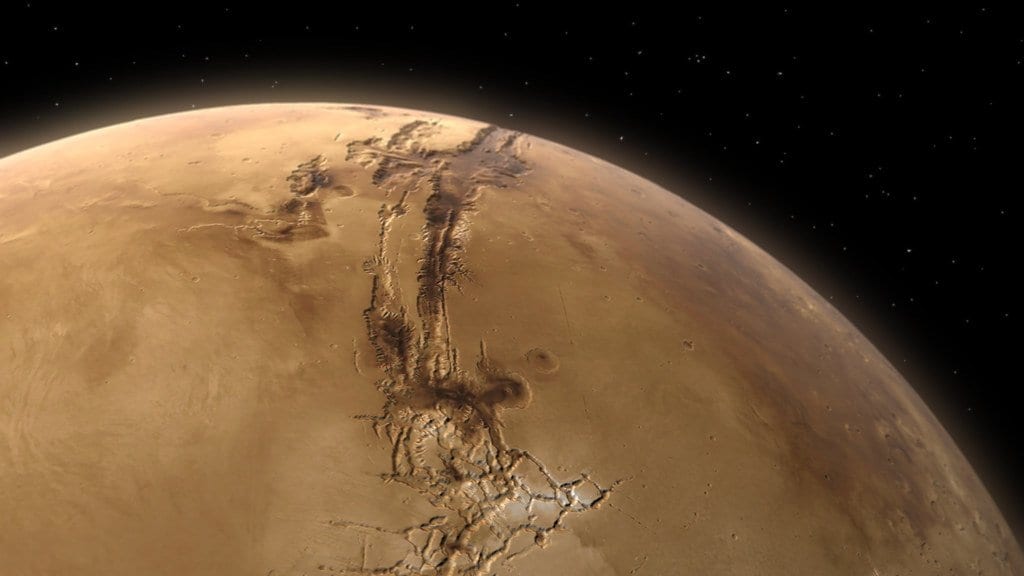 Mars seen from above the limb, with the long gash of Valles Marineris running across the orange disk.