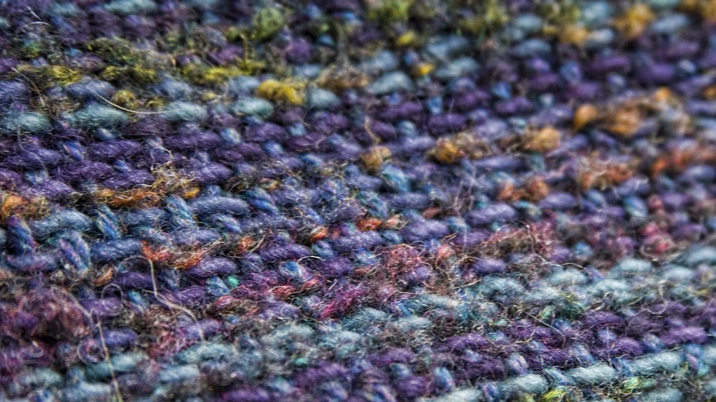 Macro photograph of woven wool cloth in purple, blue and ocher yarn, with the individual threads crossing over and under one another.