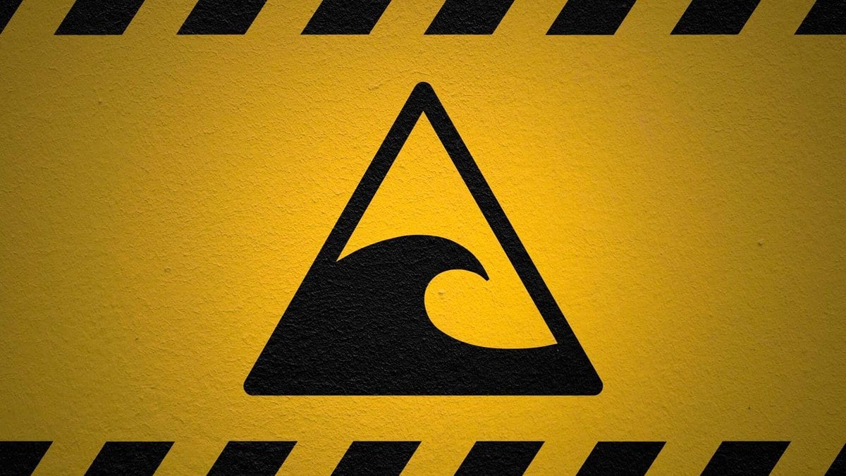 A black tsunami wave symbol inside a triangle, painted on a yellow wall framed by black and yellow hazard stripes.