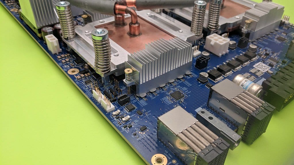 Close-up of a Google TPU v3 accelerator board, with copper liquid-cooling pipes and metal heat sinks mounted on a blue circuit board.