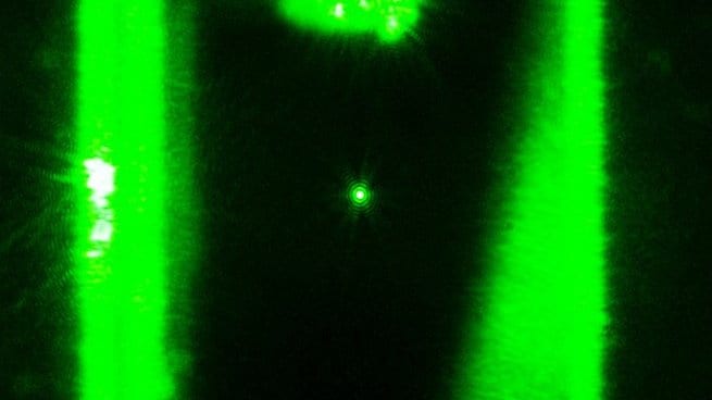 A tiny bright point of scattered light between two vertical green laser beams: a nanoparticle held in an optical trap.