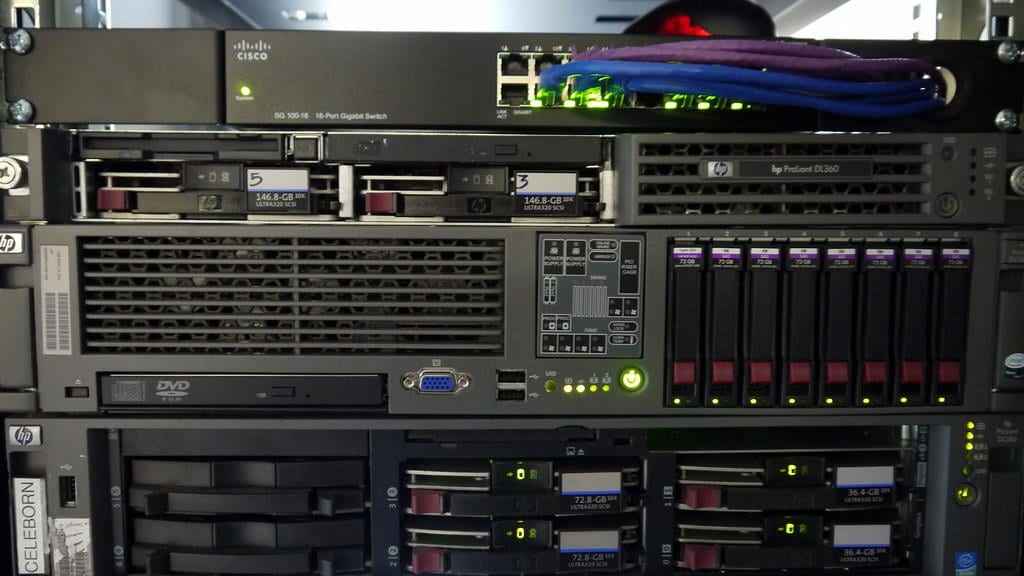 Rack-mounted servers and a network switch with lit status lights in an equipment rack.