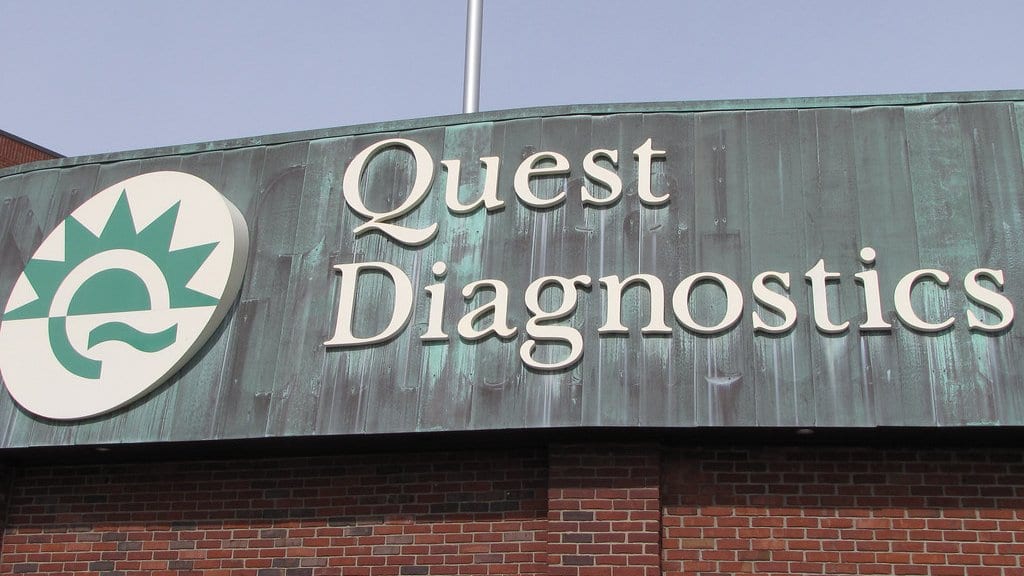 A large building-mounted sign reading Quest Diagnostics, with the company logo, above a brick wall.