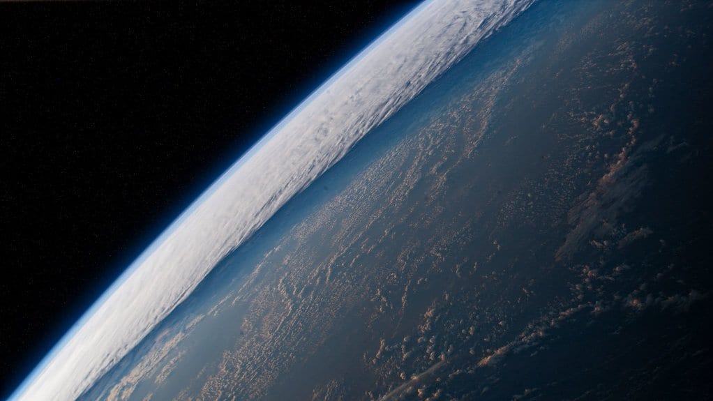 Earth's curved limb seen from orbit, with sunlit bands of cloud scattered over the dark blue water of the Pacific Ocean.
