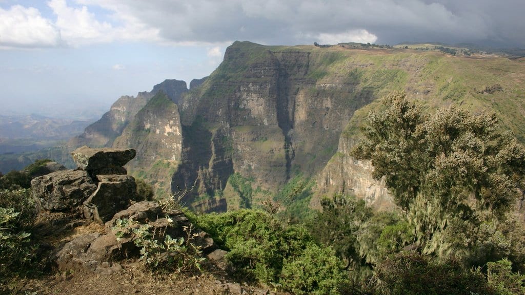 A steep rock escarpment in the Ethiopian highlands, with heavy cloud above and hazy lowland plains in the distance.
