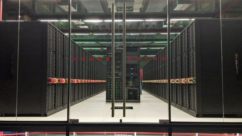 Two long rows of black computing cabinets facing each other across a narrow aisle in a machine hall.