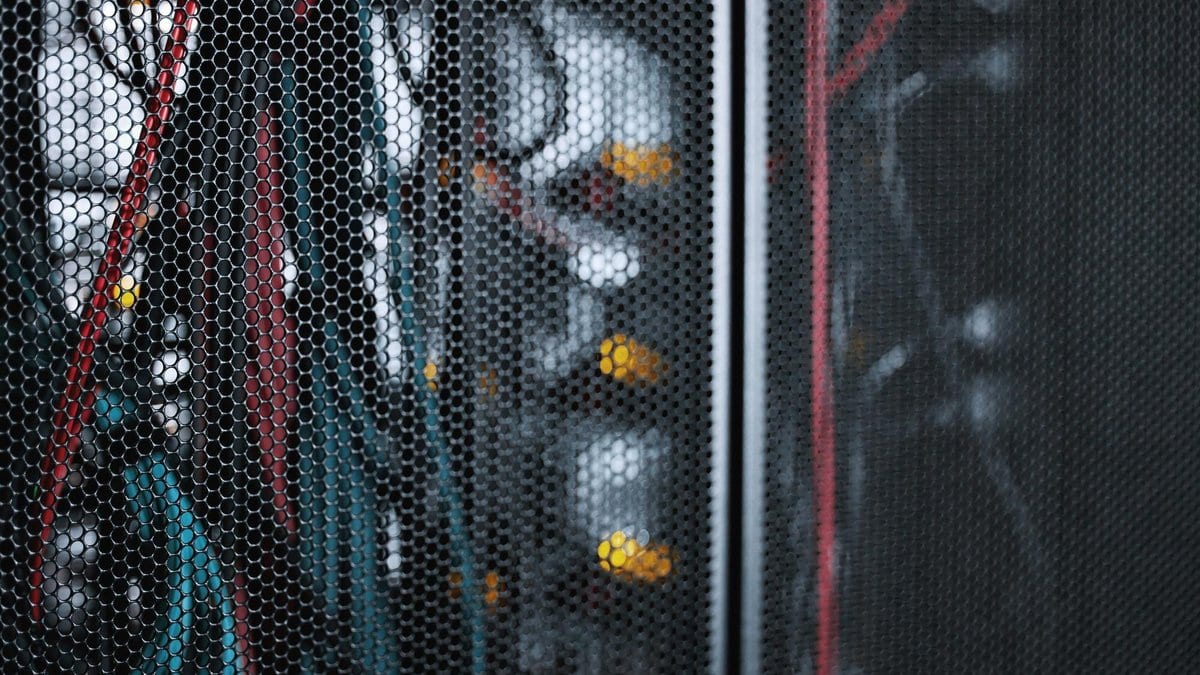 Cables and amber status lights seen through the perforated mesh door of a server cabinet.