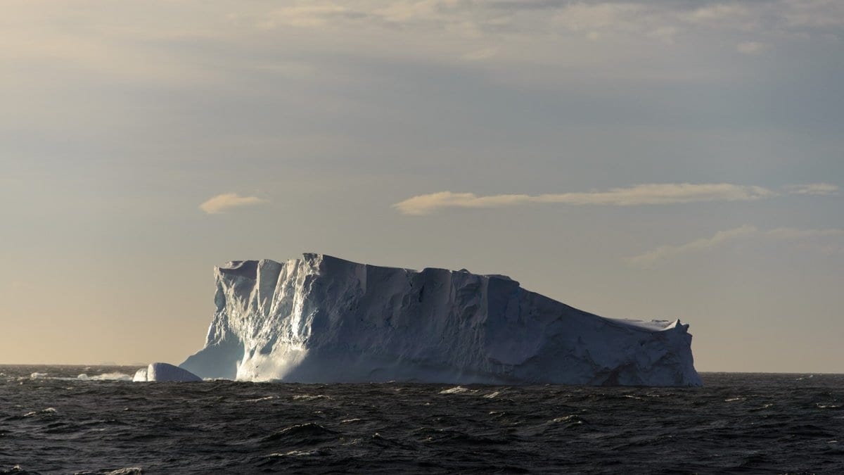 A flat-topped tabular iceberg floating in dark open ocean under a pale sky.