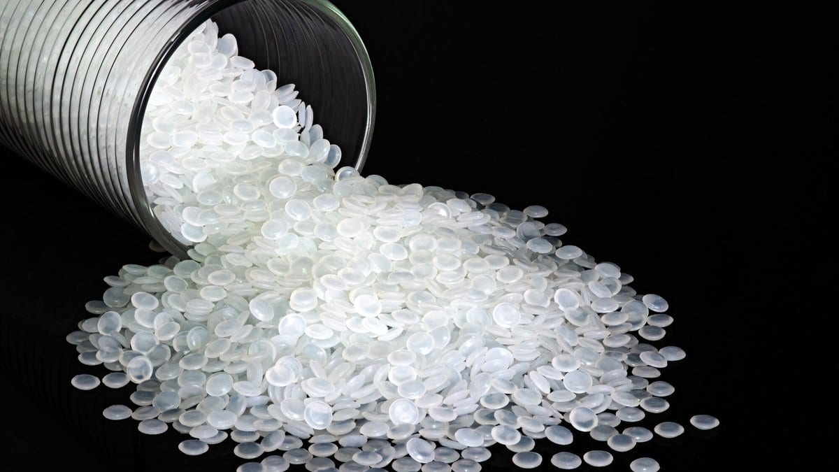 White translucent plastic pellets spilling from a tipped glass jar onto a black surface.