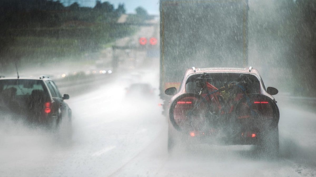 Cars and a truck driving through heavy rain on a wet multilane road, with spray rising from the pavement.