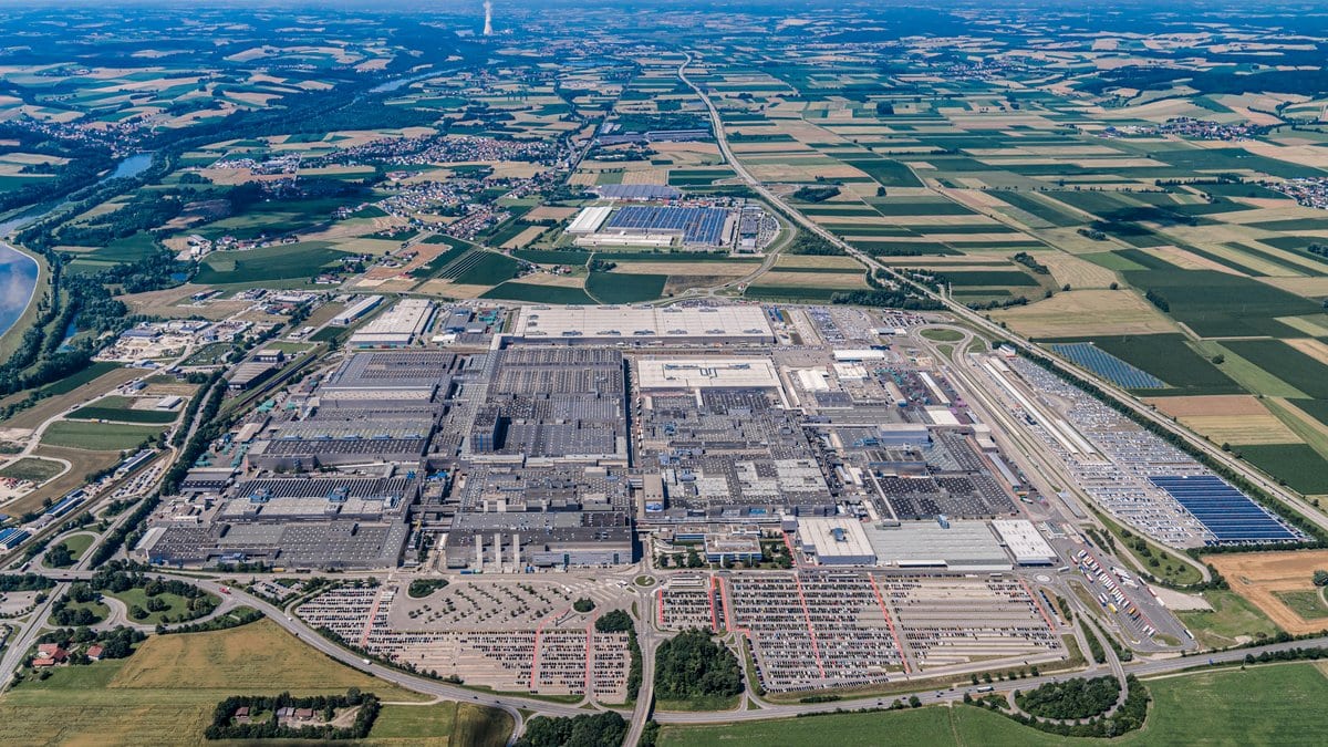 Aerial view of the BMW Group plant at Dingolfing, a dense block of production halls ringed by parking areas full of cars and by Bavarian farmland.