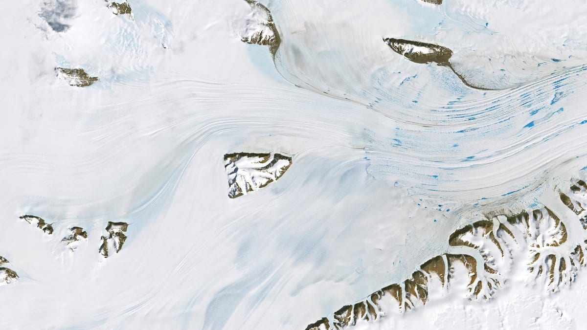 Satellite view of Antarctic ice streams flowing between bare rock ridges, with faint blue meltwater on the white ice.