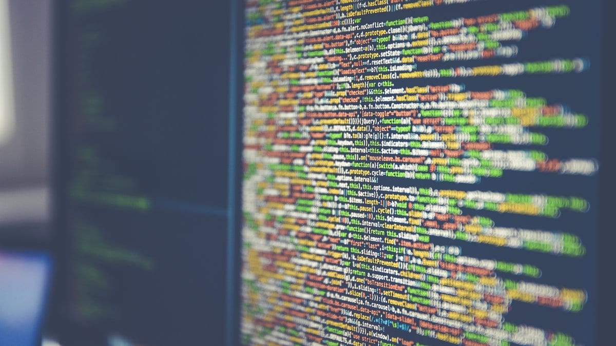 Lines of colored program code filling an angled computer monitor, with a second screen behind it.