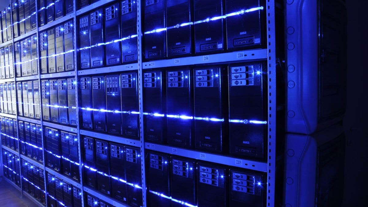 An aisle of rack-mounted servers lit by rows of blue indicator lights inside a data center.