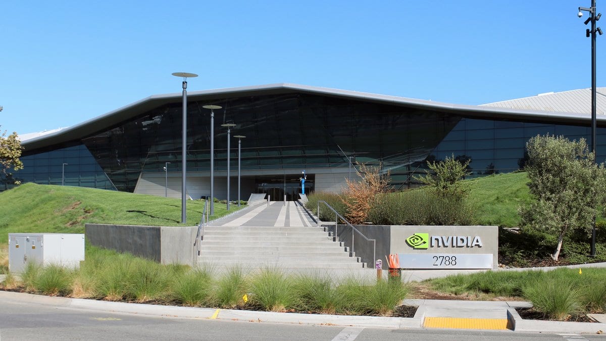 A low, angular glass office building with a sloping dark roof, fronted by a concrete stairway and a roadside sign reading NVIDIA 2788.