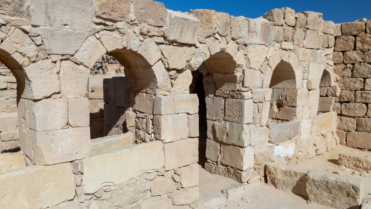 Standing ruins at Shivta: a stone facade with four arched openings, built of large squared blocks with smaller rough stones between them, under a clear blue sky.