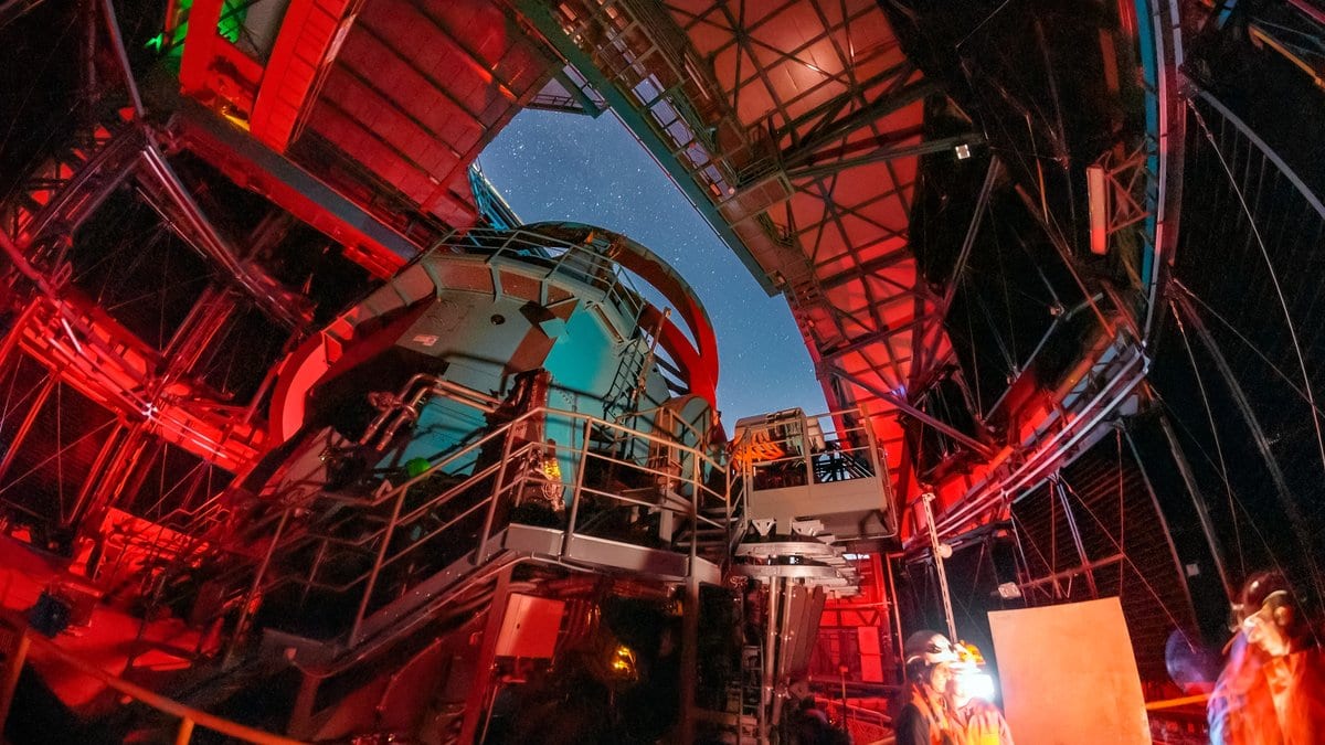The Simonyi Survey Telescope inside its dome at night, lit in red, with stars visible through the open shutter above it.
