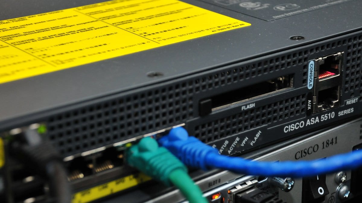 Close view of the rear panel of a Cisco ASA 5510 firewall, with green and blue Ethernet cables plugged into its network ports.