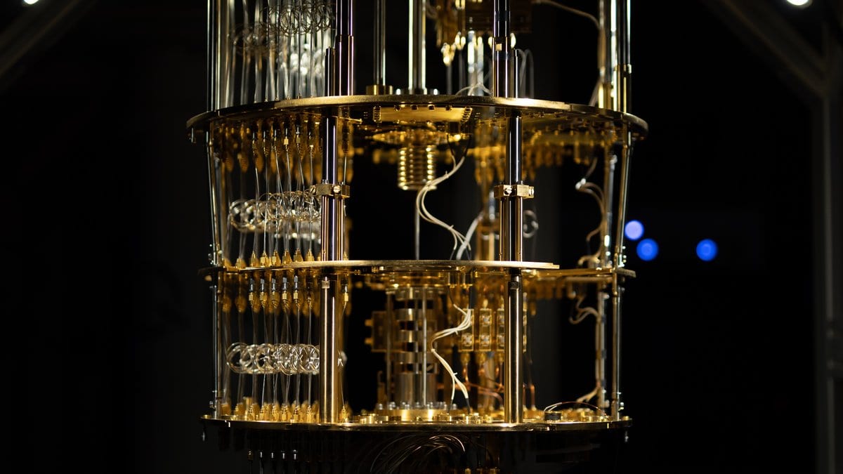 Gold plated circular stages of a dilution refrigerator hang in a dark enclosure, threaded with coaxial cables and wiring loops.