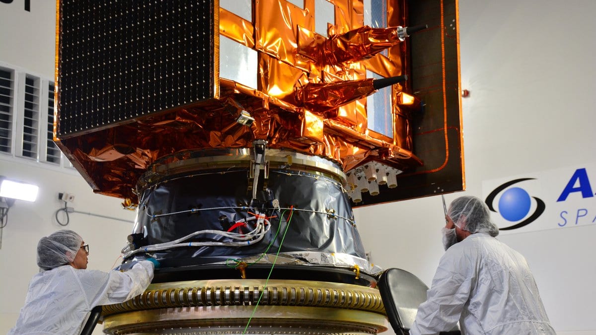 Technicians in white cleanroom suits steady the gold-wrapped Sentinel-6B satellite as it hangs above the cone-shaped adapter that will carry it on its rocket.