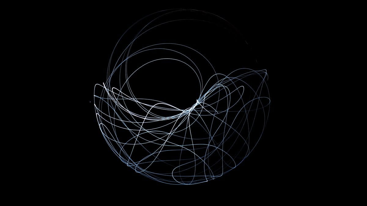 A tangle of pale blue light arcs forming a rough sphere against a black background, traced by the moving tip of a double pendulum during a long exposure.