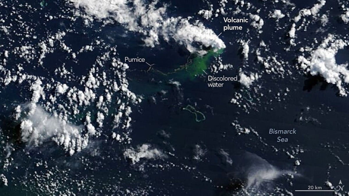 A true-color satellite view of the Bismarck Sea showing a pale volcanic plume, streaks of floating pumice and bright green discolored water above a submarine vent, with scattered cloud across the scene.