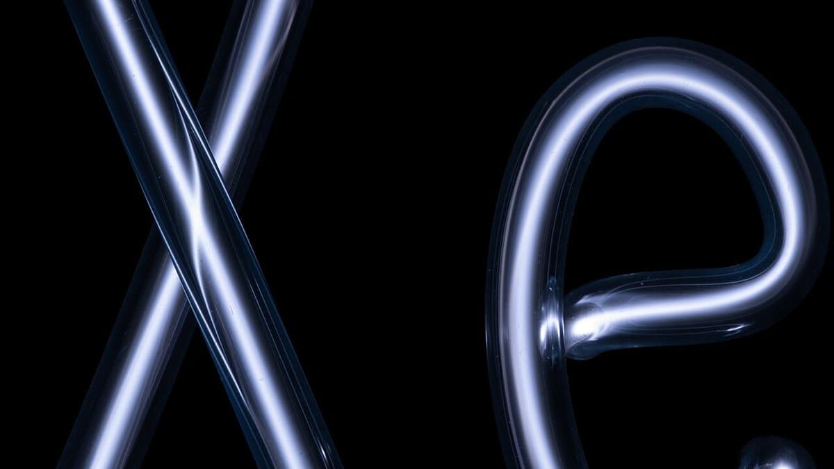 A glass discharge tube bent into the chemical symbol Xe, glowing pale blue-white with ionised xenon