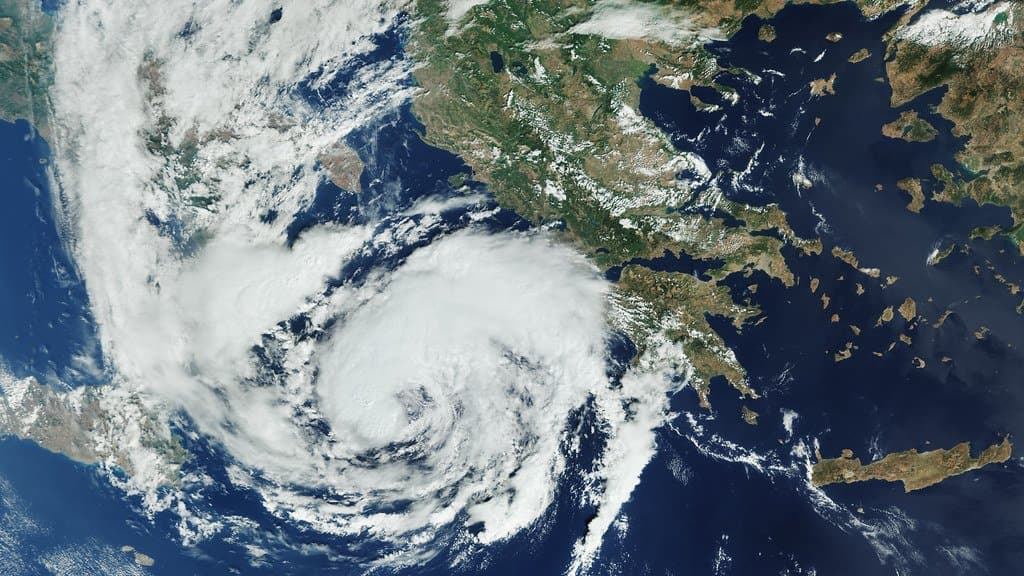 A satellite view of the central Mediterranean with a tightly wound spiral of white cloud sitting over the Ionian Sea west of Greece.
