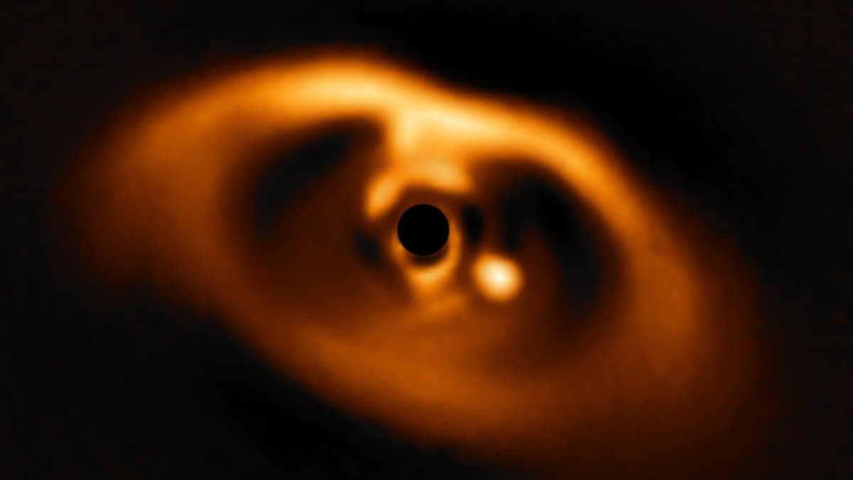 A glowing orange ring of dust surrounds a black disc masking the central star, with a bright point of light sitting inside the gap in the ring.