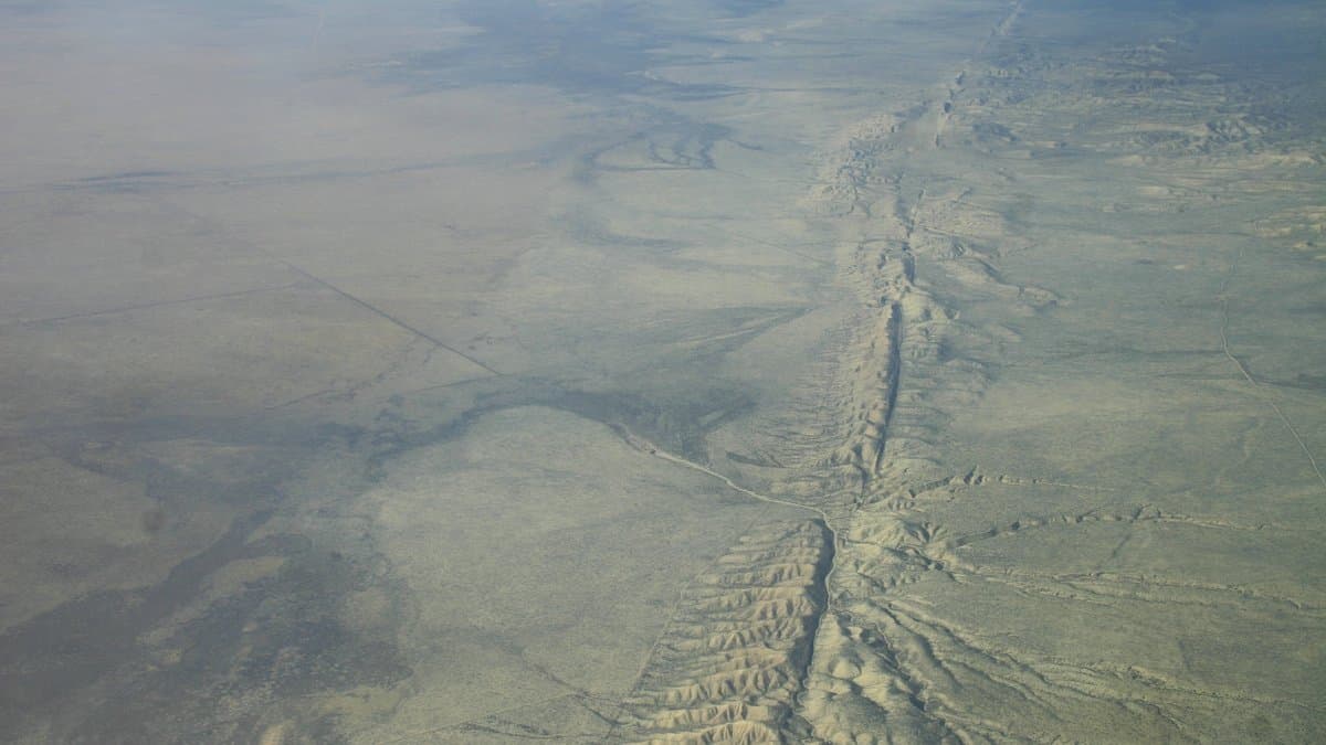 Aerial photograph of the San Andreas fault trace running as a straight crease across the dry grassland of the Carrizo Plain in California, with low ridges on either side of the line.