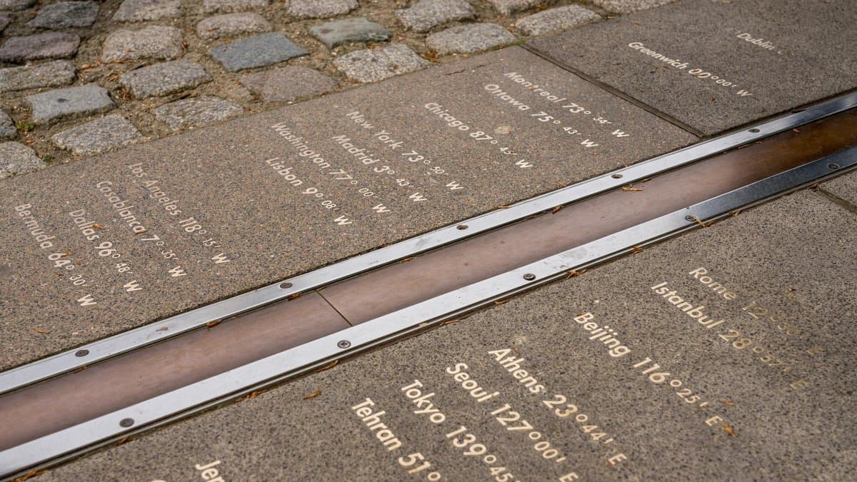 A brass and steel strip set into stone paving marks zero degrees longitude at the Royal Observatory in Greenwich, London. City names and their longitudes east and west are engraved in the stone on either side.