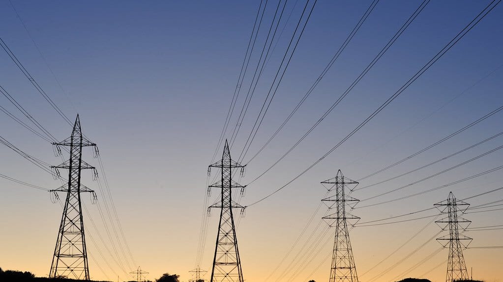 Four high-voltage transmission towers of different sizes silhouetted against a dusk sky, linked by many power lines