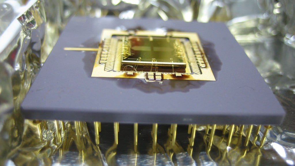 Macro photograph of a gold wire-bonded surface ion trap chip mounted on a ceramic carrier and resting on metal foil.