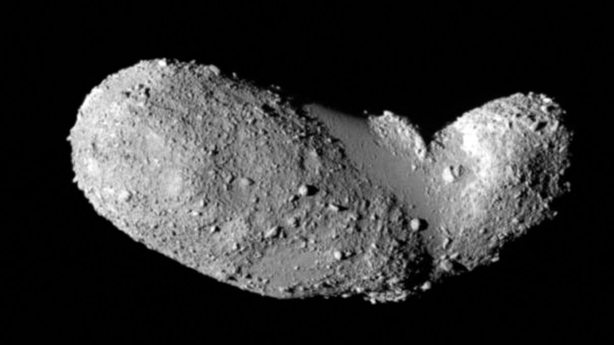 Elongated gray asteroid Itokawa against black space, its two lobes covered in loose boulders and gravel.