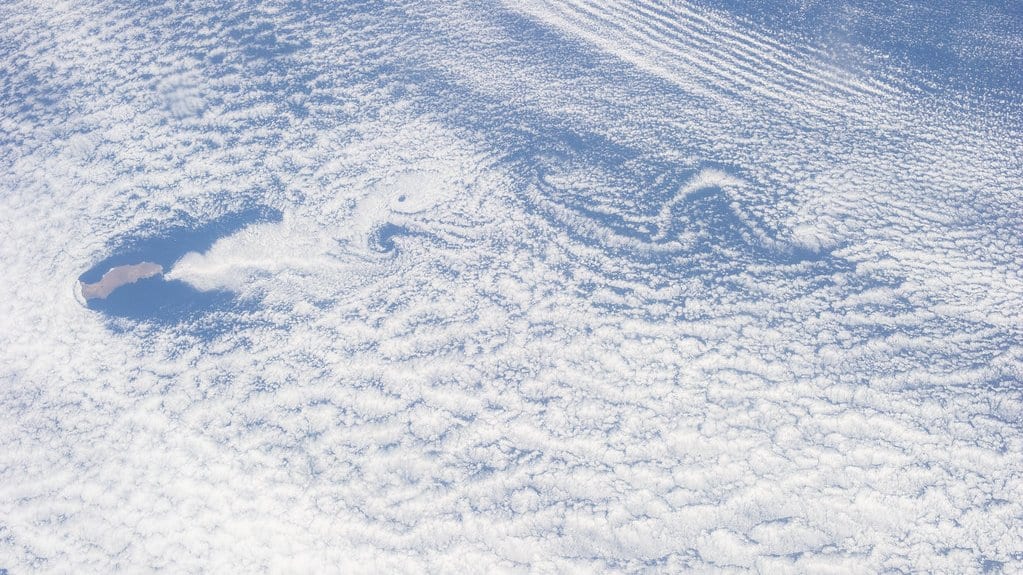 Satellite view of a wide deck of low cloud over the ocean, with a line of spiral eddies trailing downwind from a small island.