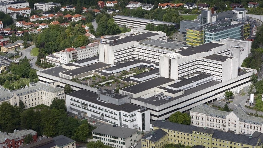 Aerial view of the Haukeland University Hospital complex, long gray and white buildings set among trees on a hillside in Bergen, Norway.
