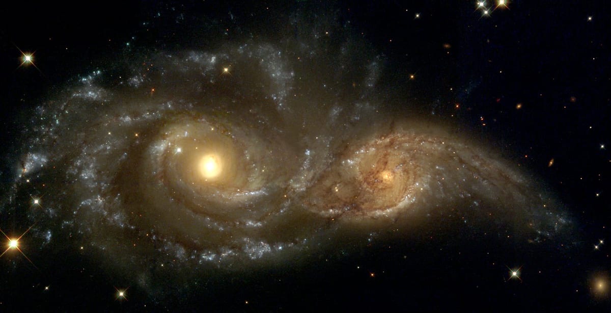 Two spiral galaxies passing close to each other, their arms drawn out and overlapping against a black field of stars.