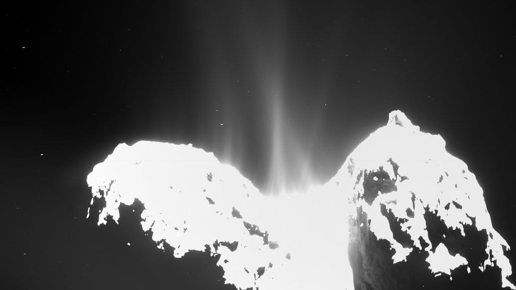 The brightly lit two-lobed nucleus of comet 67P/Churyumov-Gerasimenko at the base of the frame, with pale jets of gas and dust rising from the neck between the lobes into black space.